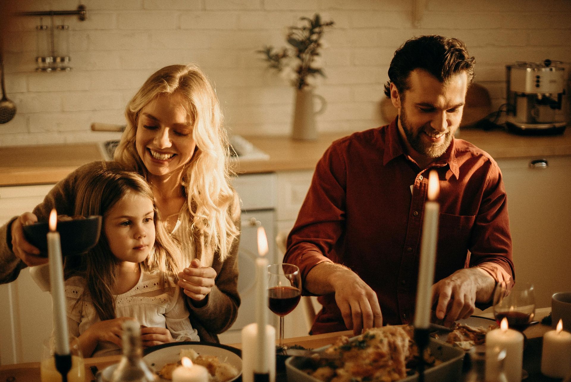Family cooking together in a warm kitchen, with candles lit on a festive table.