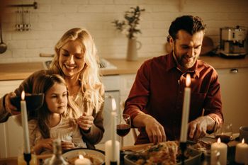 Family sharing a candlelit meal at a dining table, with a woman, child, and man in warm kitchen light