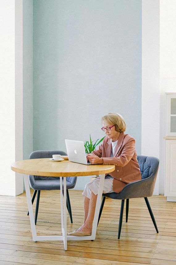 Person working on a laptop at a round table in a bright room with a flower vase