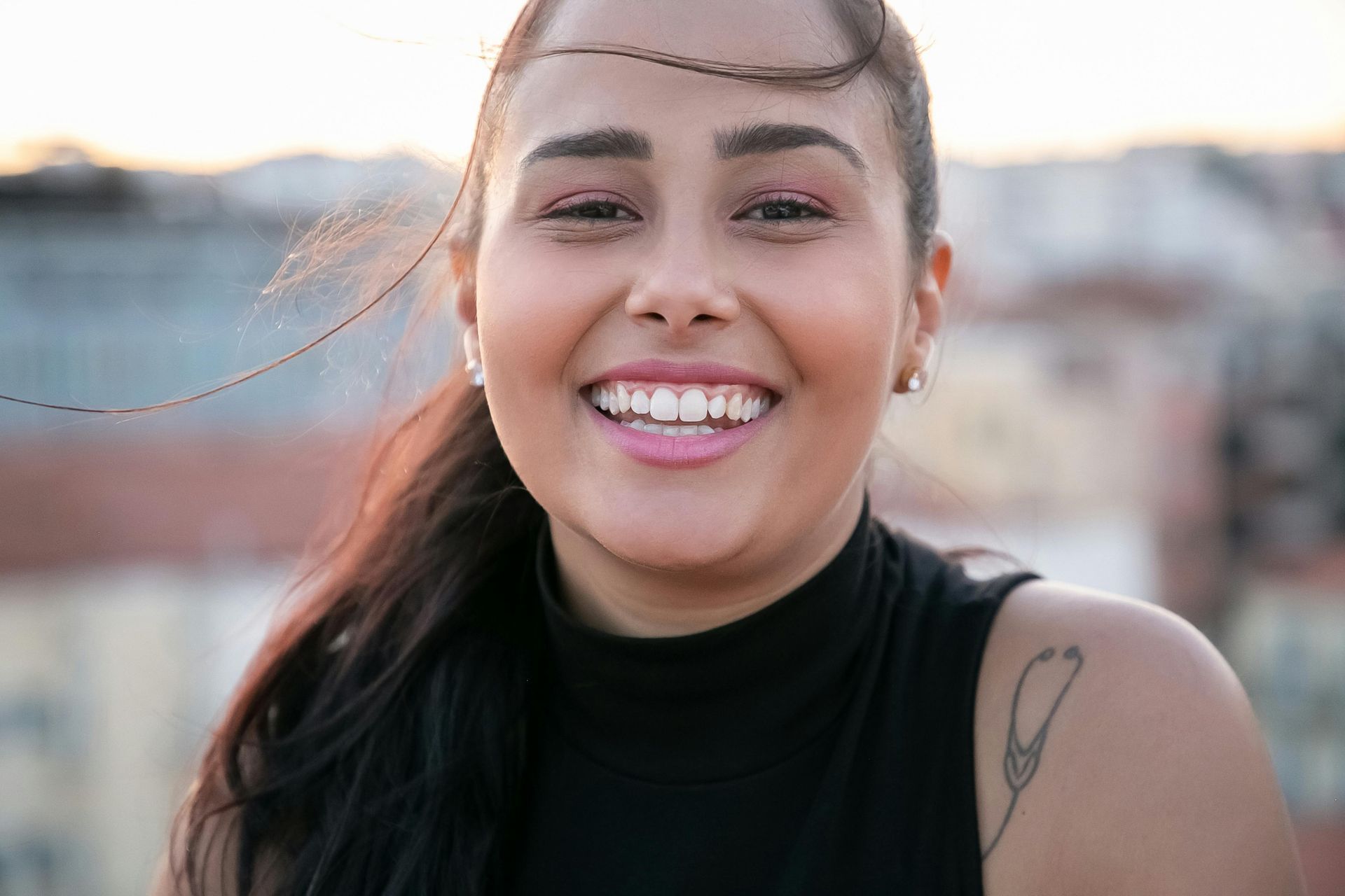 Smiling person with dark hair and a black top outdoors at sunset
