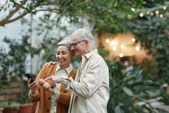 Two people smiling and pointing at a tablet in a garden with warm lights in the background