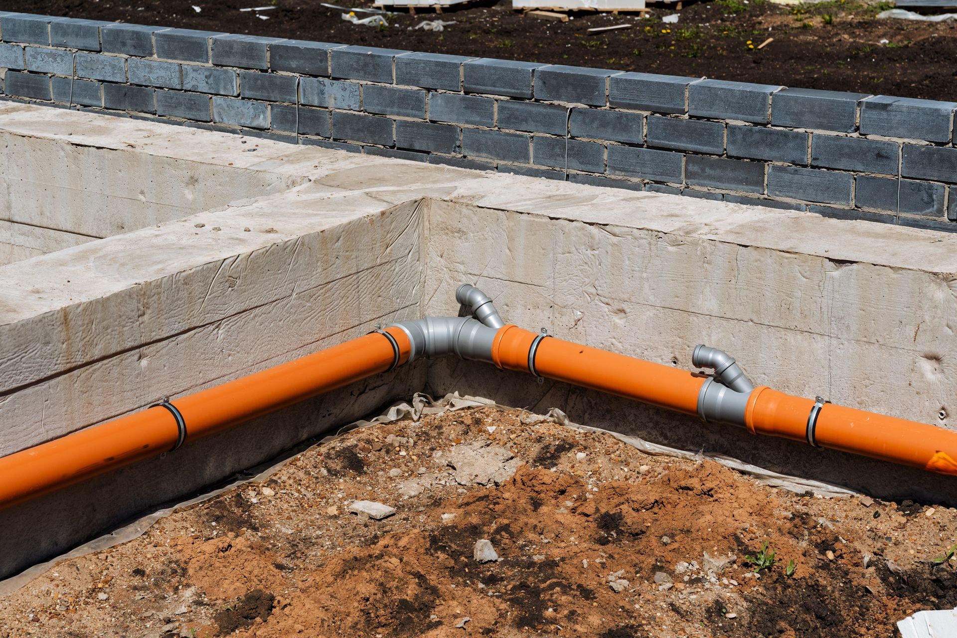Installation details of orange drainage pipelines within concrete foundation corners and trenches