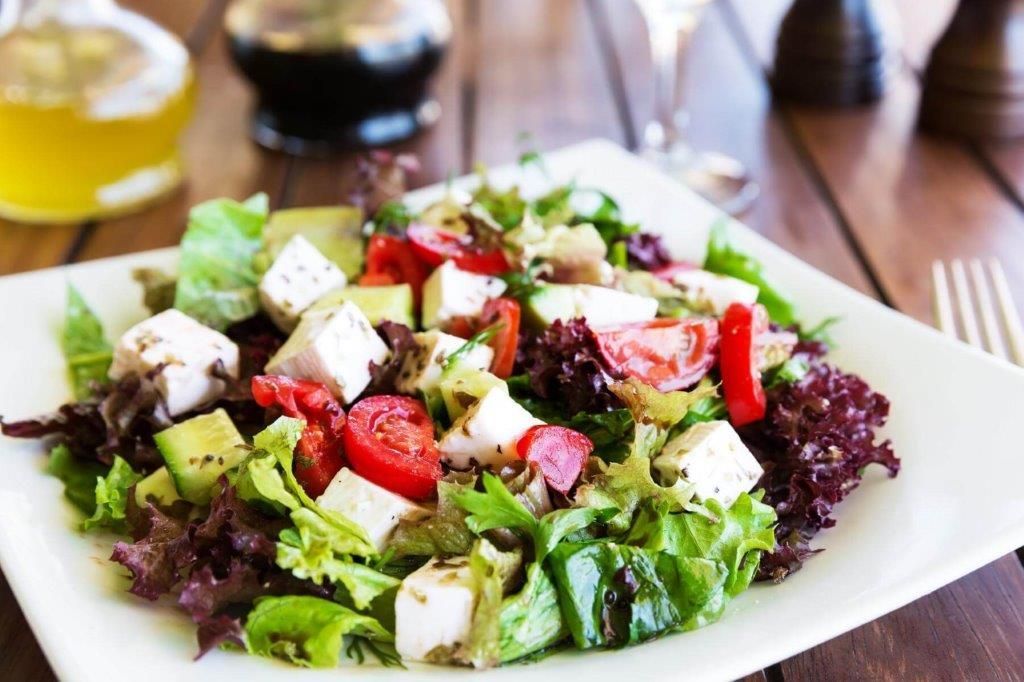 Un piatto bianco condito con un'insalata di lattuga, pomodori e formaggio