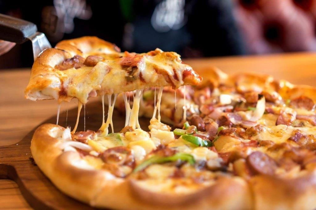 Una persona sta prendendo una fetta di pizza da una tavola di legno.
