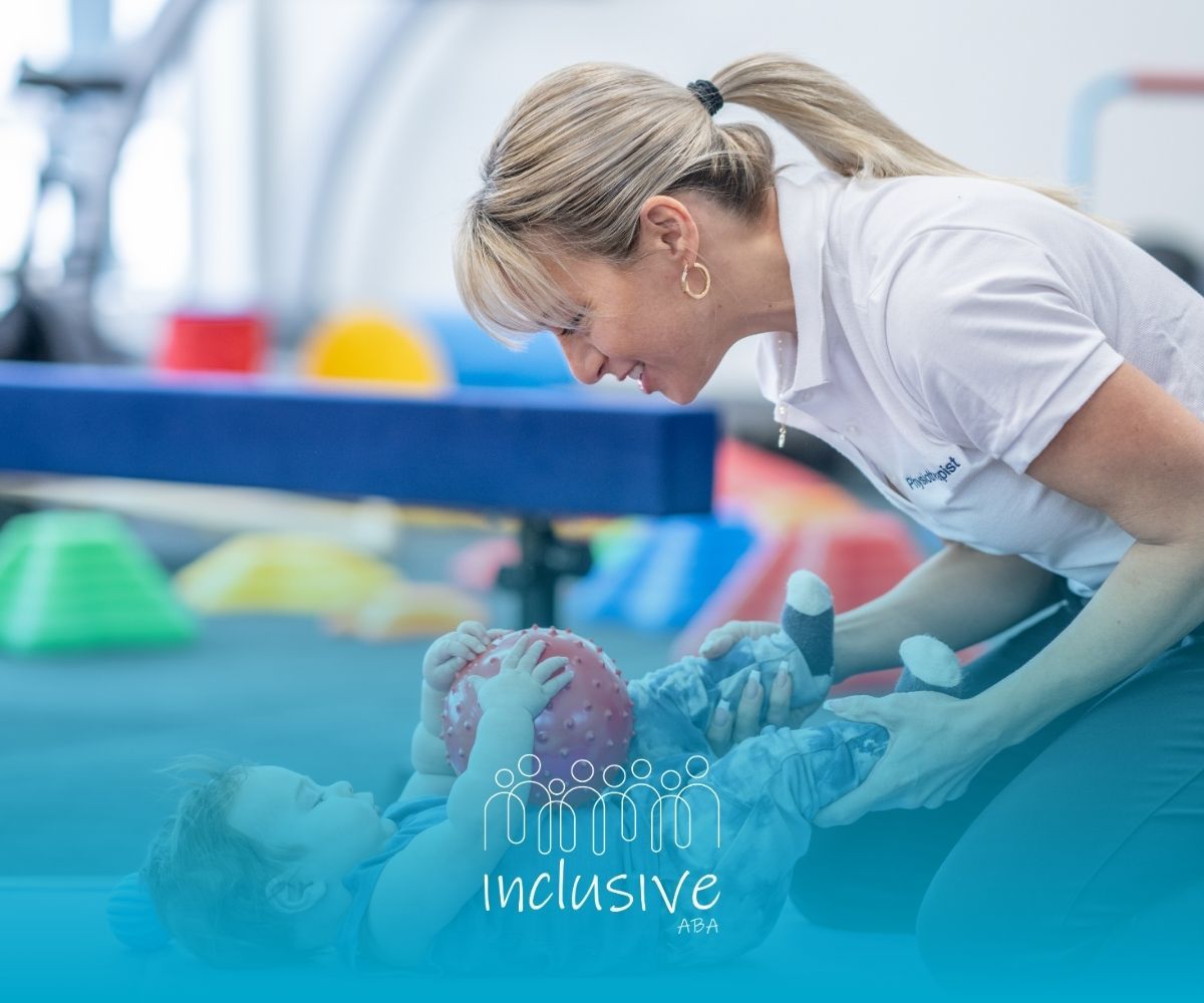 Caregiver leaning over a child on a gym mat, helping them play with a red ball in a colorful playroom