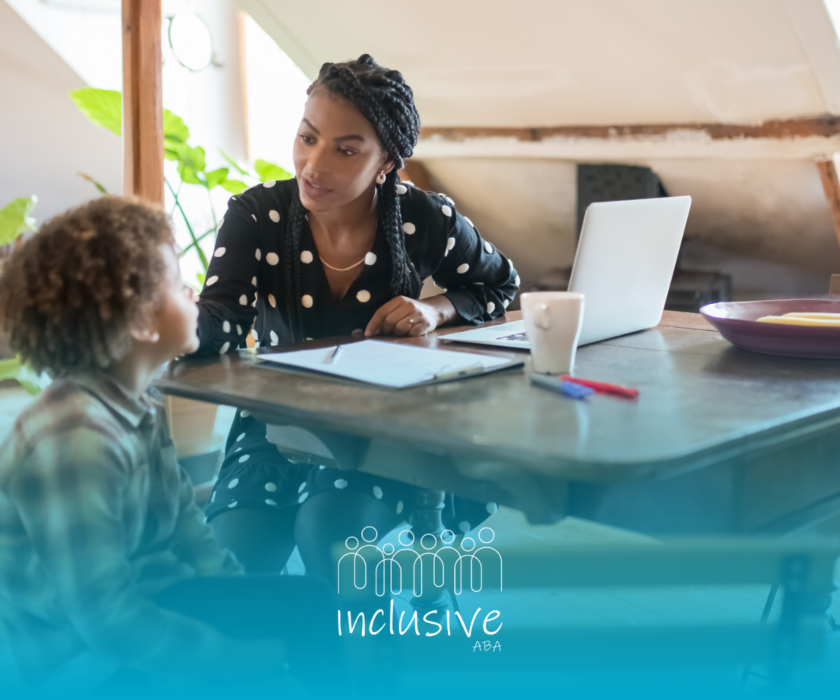 Woman talking with a child at a table with a laptop, notebook, and cup in a bright room