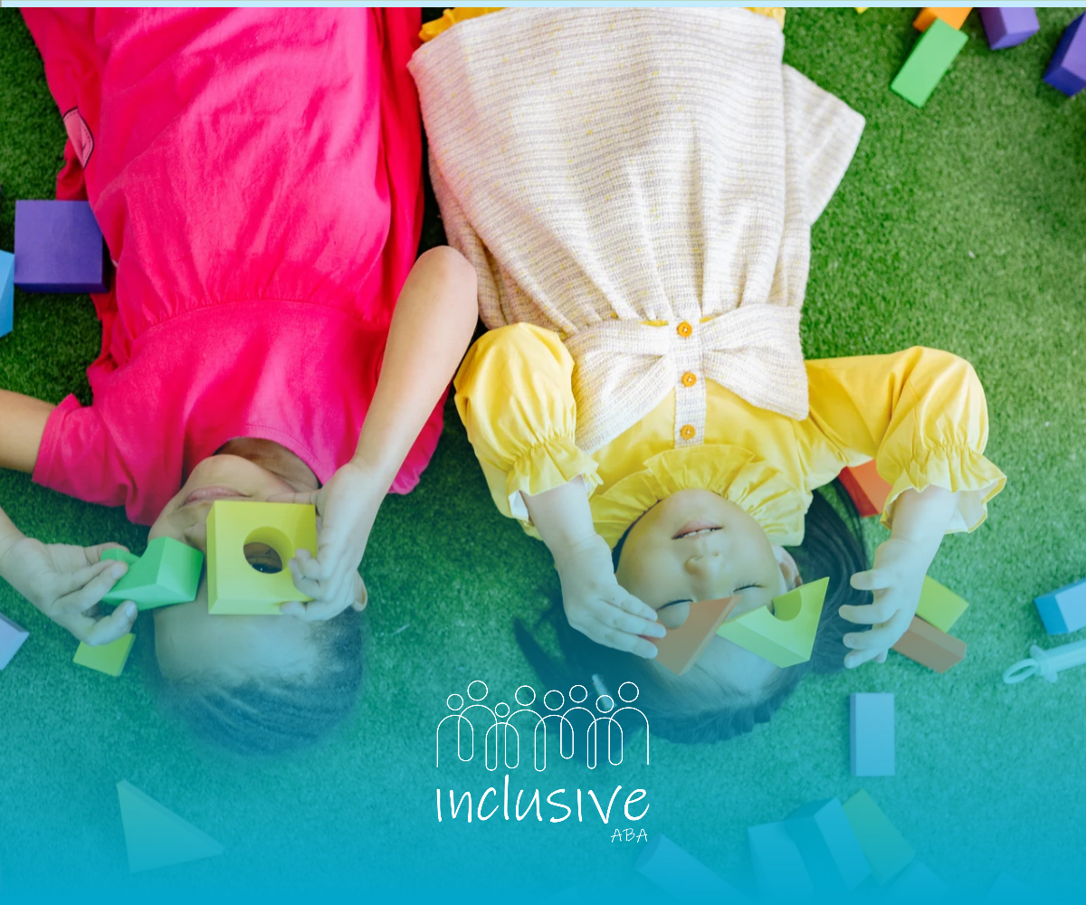 Two kids lying on grass, holding hands with a child; bright colorful blankets and toys nearby.