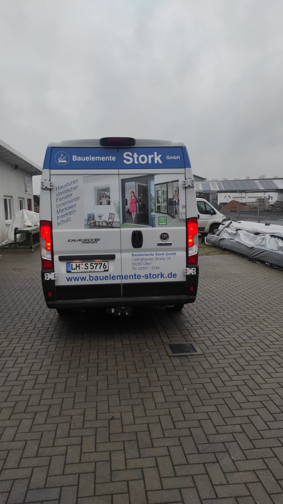 The back of a van is parked on a brick driveway.