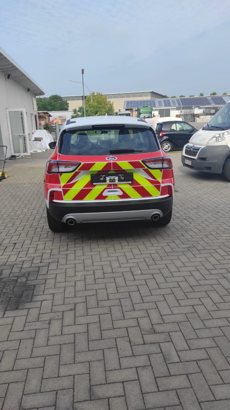 A red and yellow car is parked on a brick driveway.