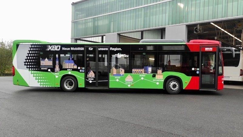 A green and red bus is parked in front of a building.