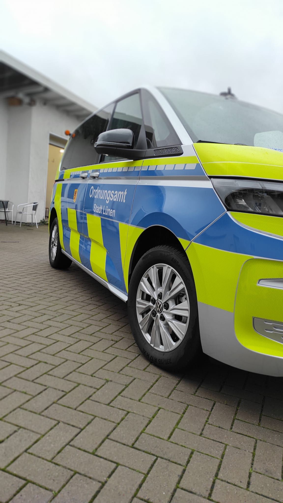 A blue and yellow police van is parked on a brick driveway.