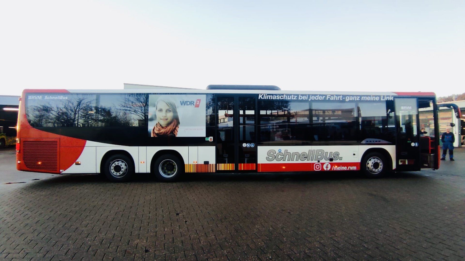 A red and white bus is parked on a brick pavement.