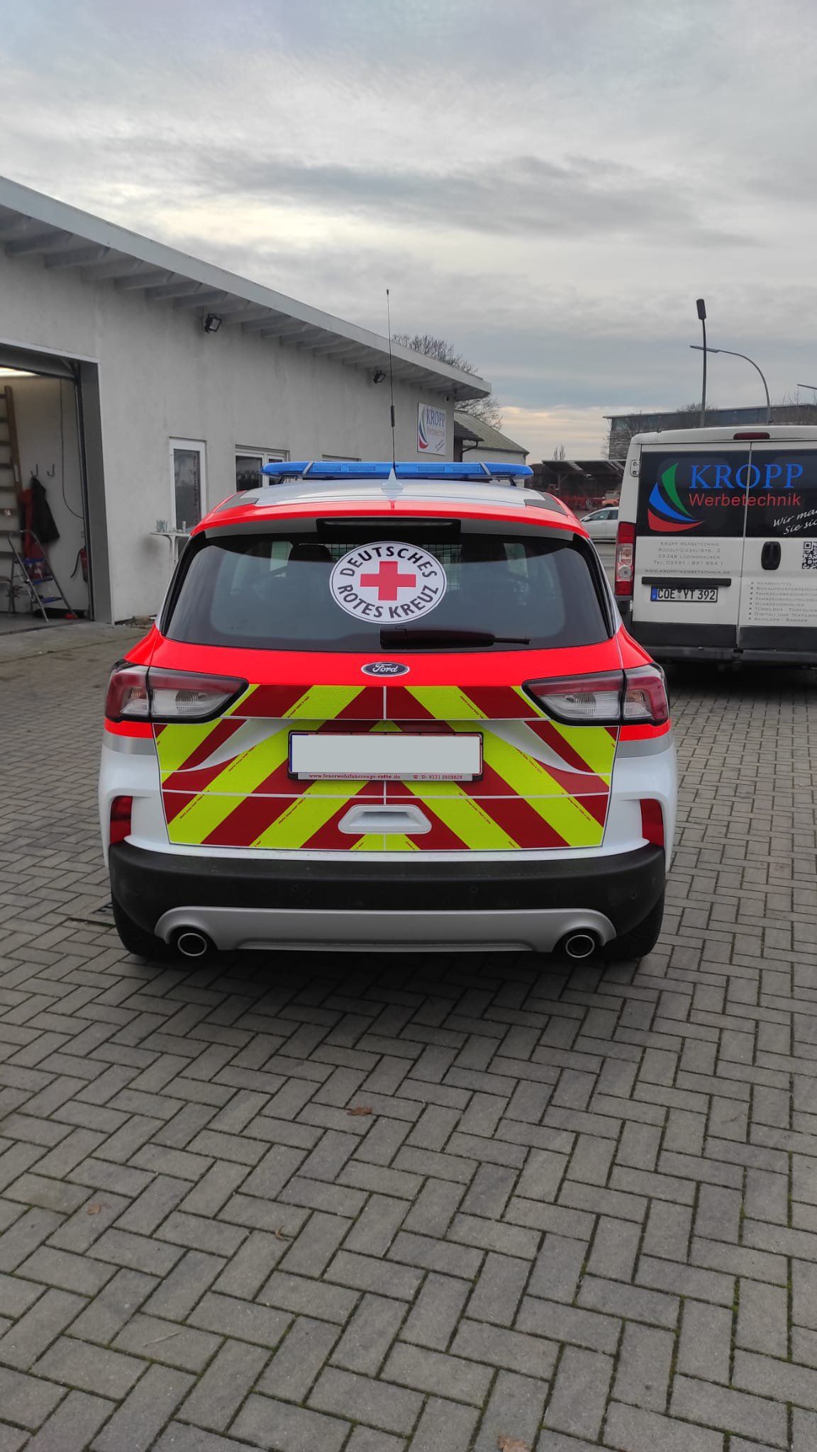 A red and yellow car with a red cross on the back is parked in a parking lot.