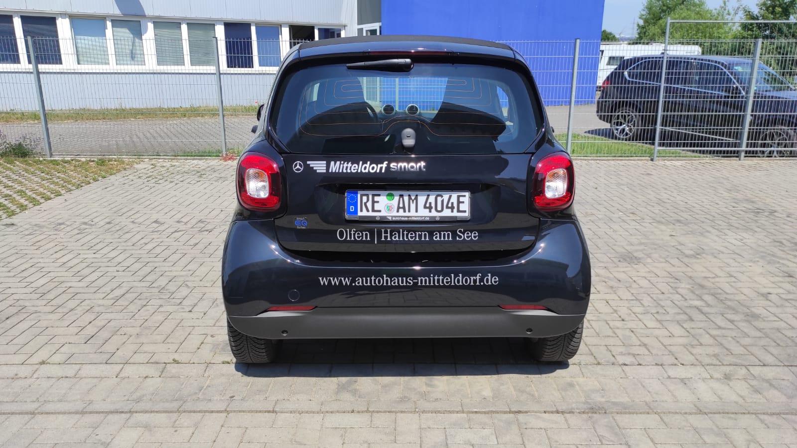 A black car is parked in a parking lot in front of a building.