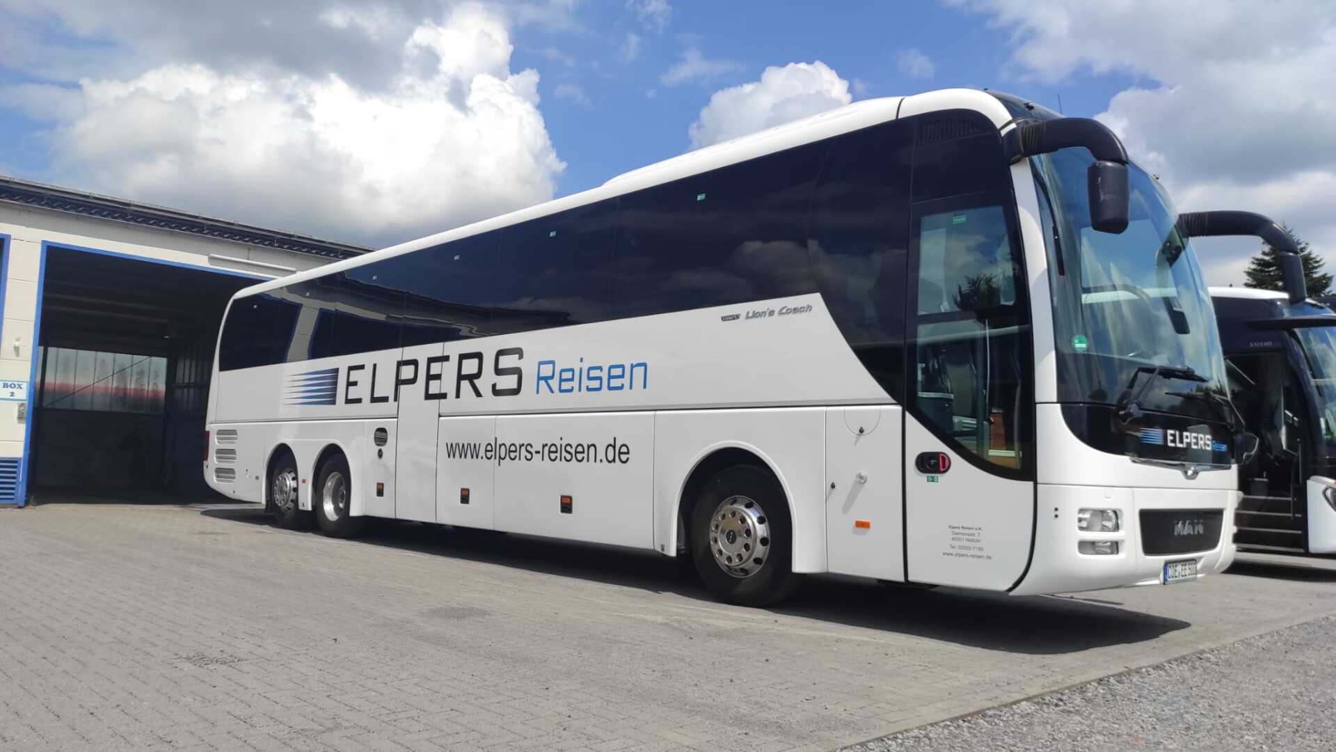 A large white bus is parked in front of a building.