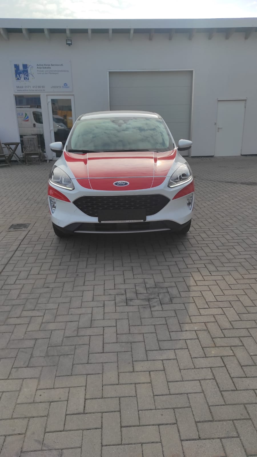 A red and white ford escape is parked in front of a building.