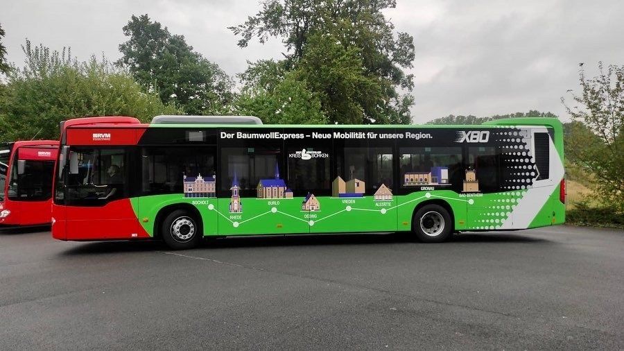 A green and red bus is parked next to a red bus in a parking lot.
