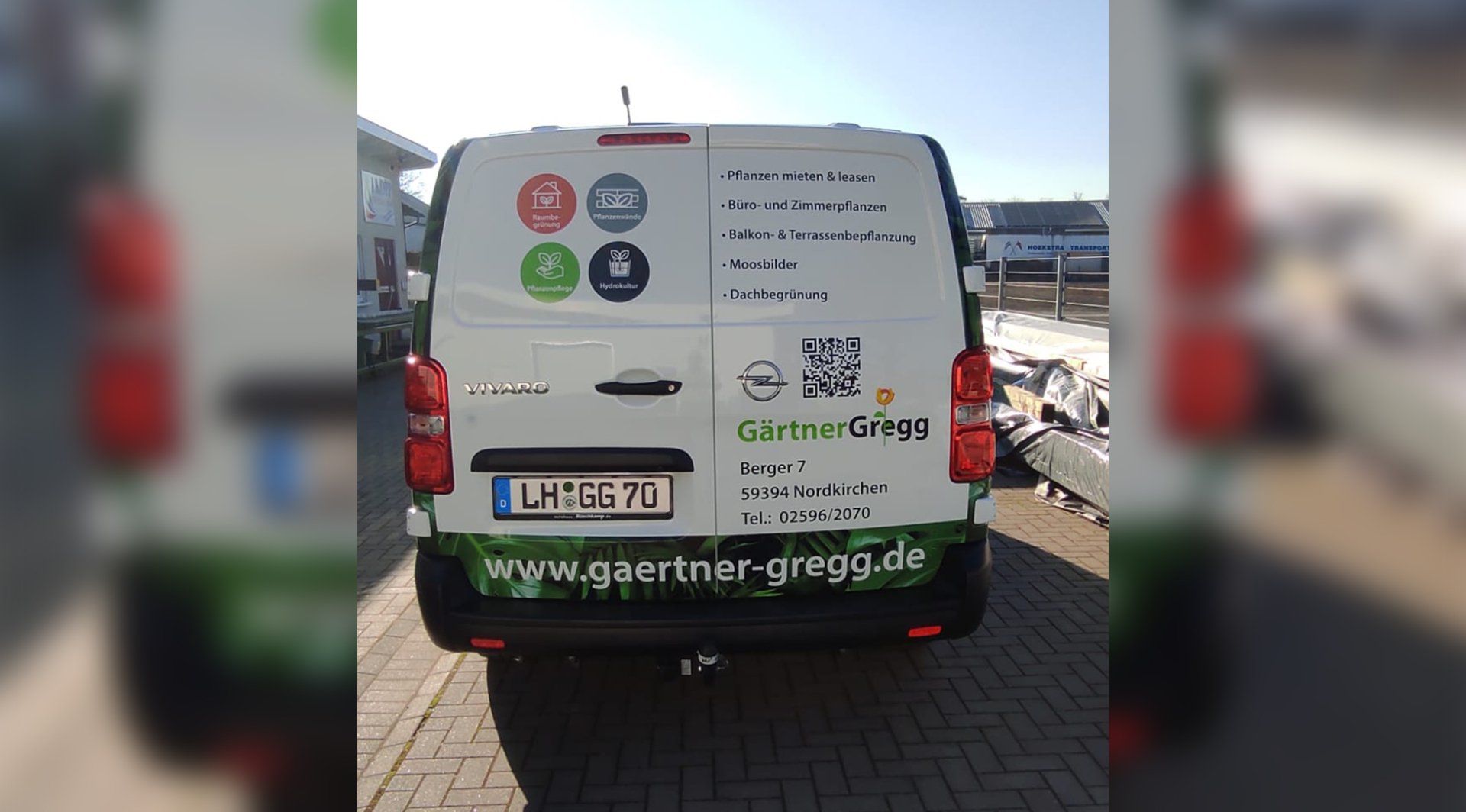 A white van with a green sticker on the back is parked on a brick sidewalk.
