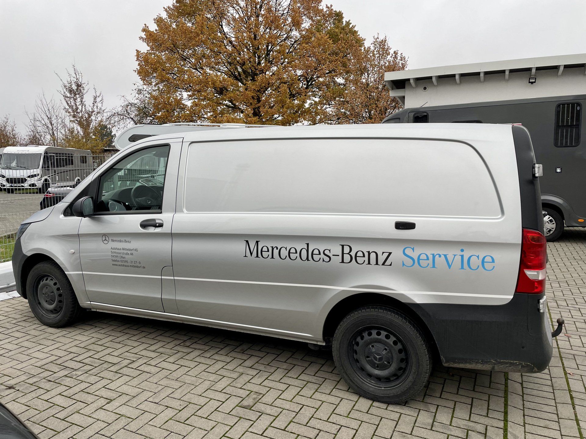 A silver mercedes benz service van is parked in a parking lot.