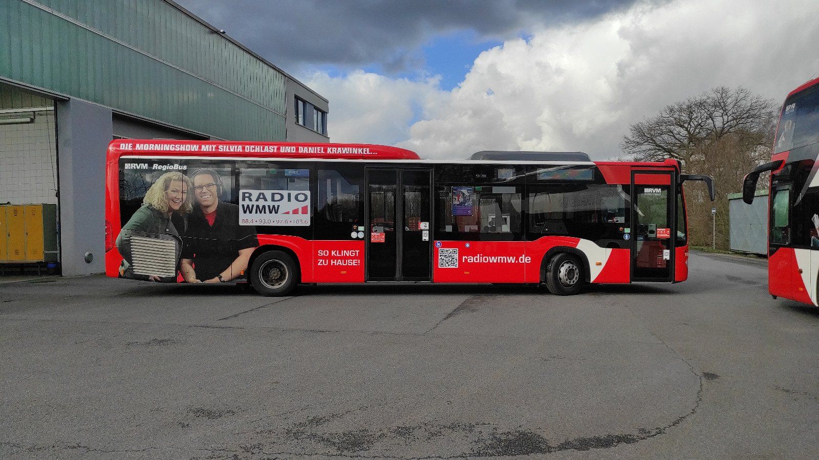 A red and white bus is parked in front of a building.