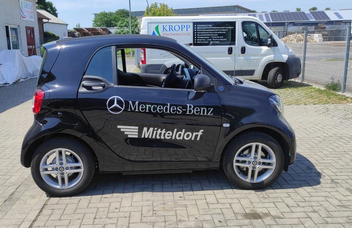 A black mercedes benz car is parked next to a white van.