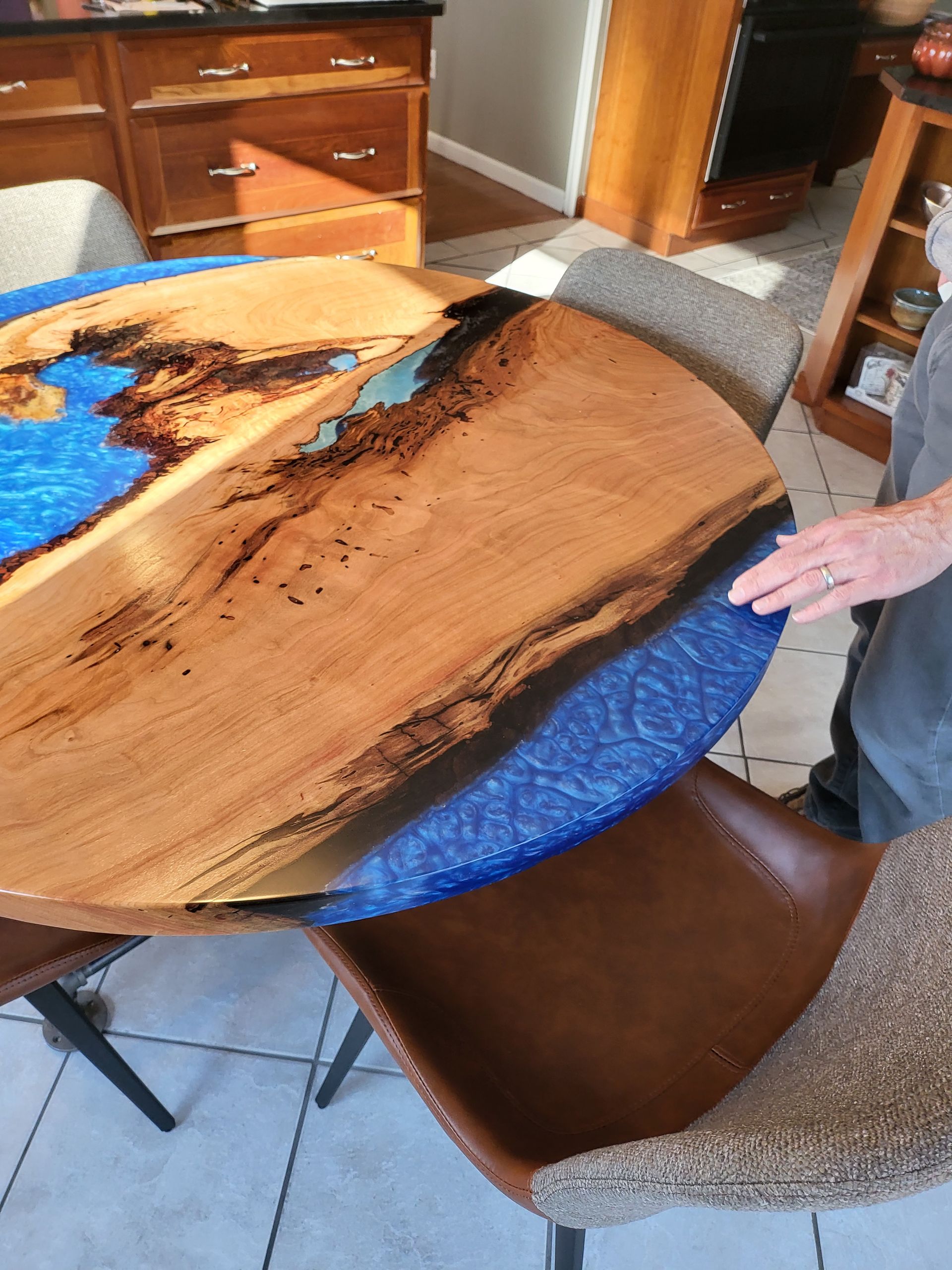 A person is standing next to a wooden table with a blue top.