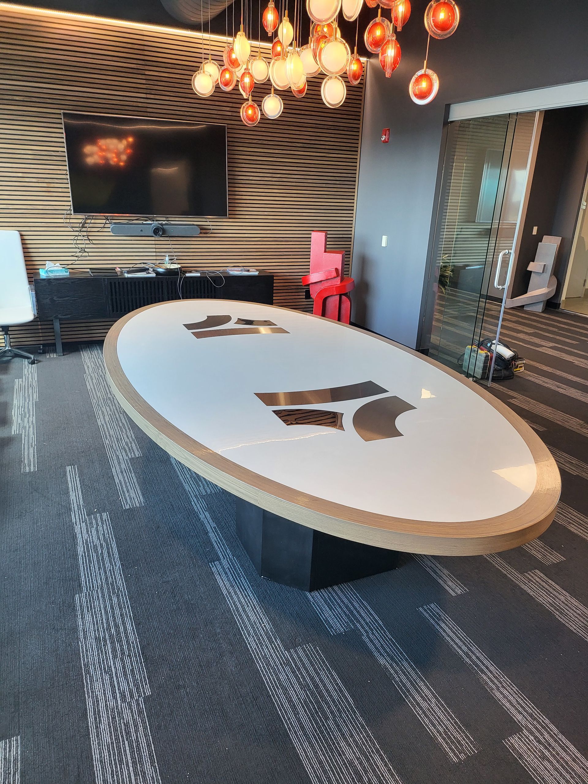 A large oval table in a conference room with a tv on the wall.