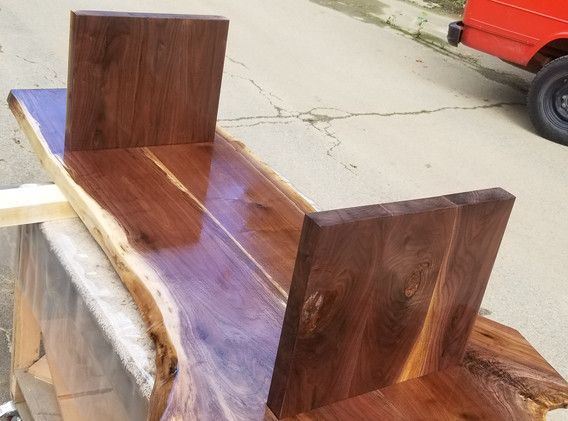 A wooden bench is sitting on the sidewalk next to a red car.