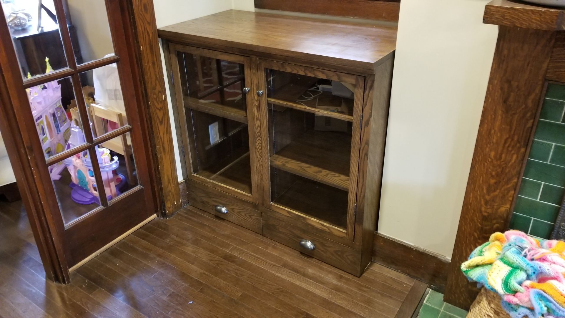 A wooden cabinet with glass doors and drawers in a living room next to a fireplace.