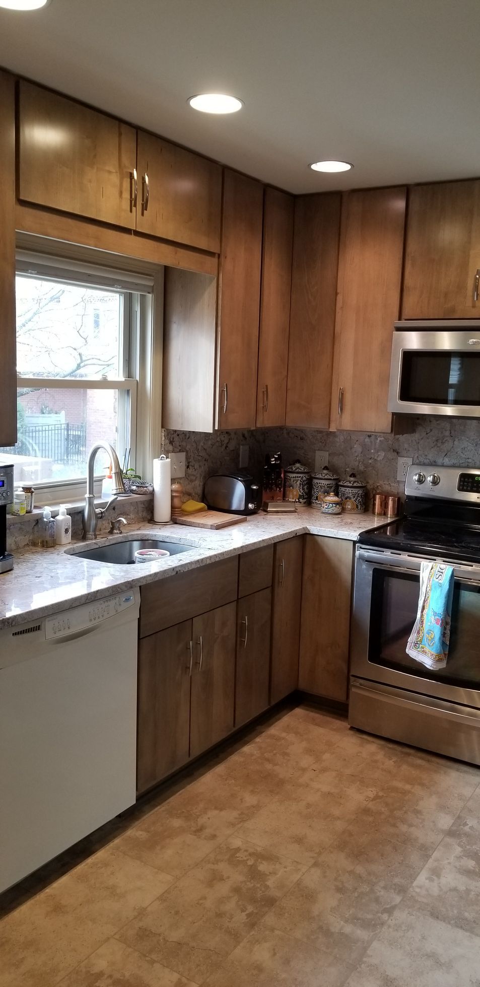 A kitchen with wooden cabinets , stainless steel appliances , a sink , and a window.