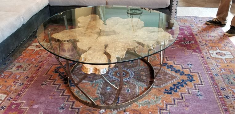 A glass coffee table with a wooden base is sitting on a rug in a living room.