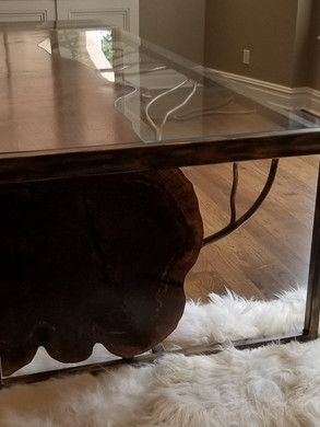 A wooden table with a glass top is sitting on a wooden floor next to a white rug.