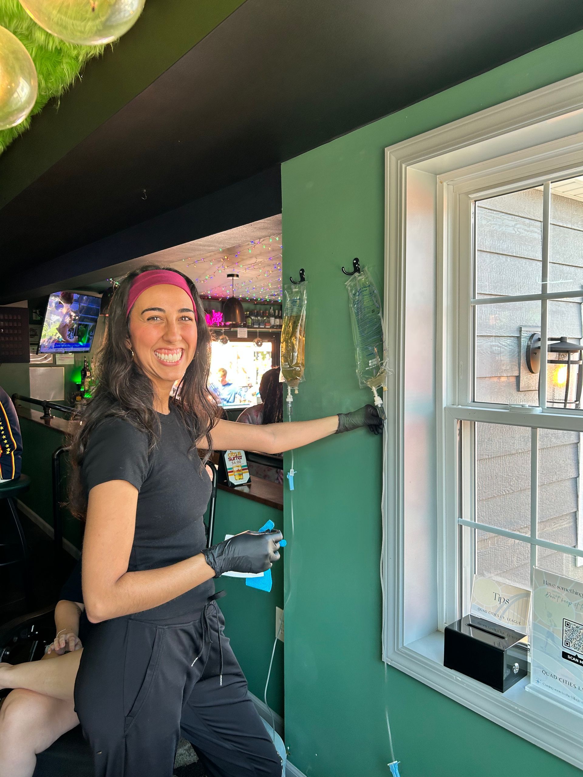 Person in black clothes and gloves painting a green wall beside a window, holding a paint roller
