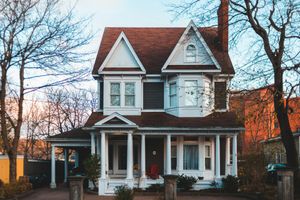 Two-story house with brown roof, white trim, and a porch. Trees flank the building.