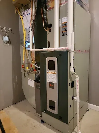 Furnace and air conditioning unit in a gray room with white PVC pipes.