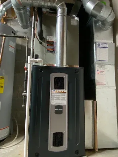 A furnace with silver exhaust pipes in a basement next to a hot water heater.