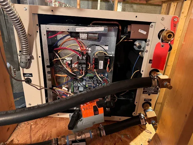 Open view of the internal components of a heating system with wiring, pipes, and control panel.