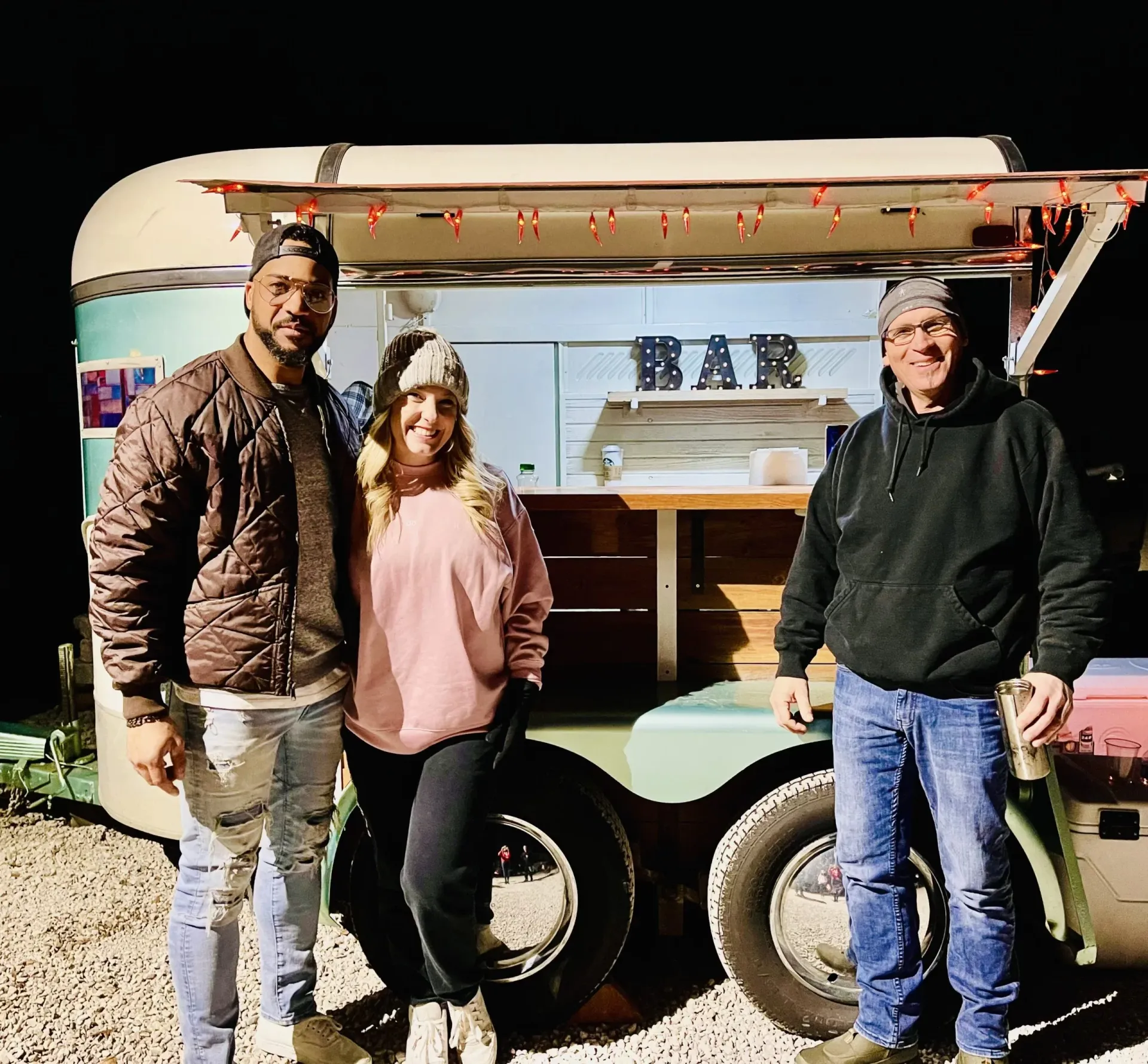 Three people standing in front of a trailer that says bar