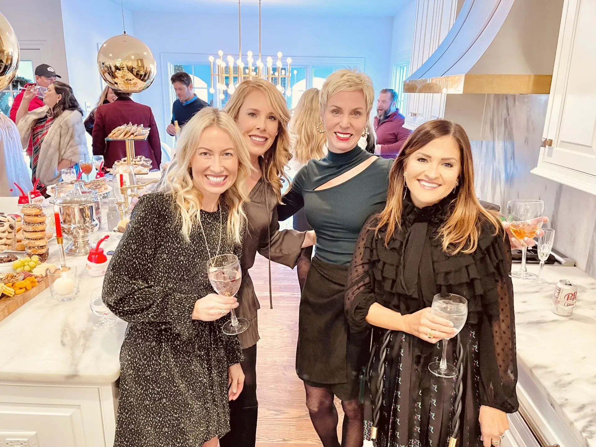 A group of women are standing next to each other in a kitchen holding wine glasses.
