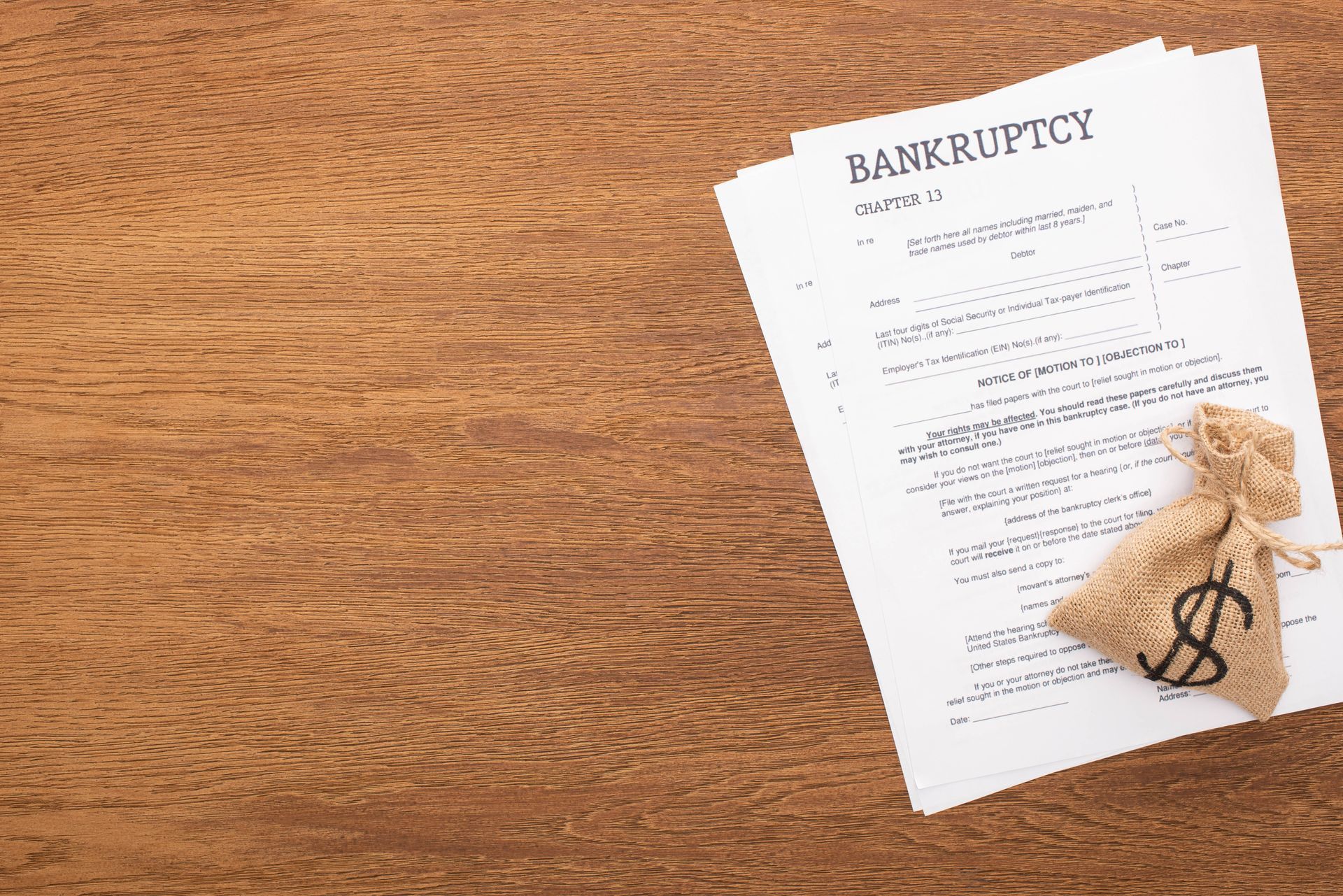 Bankruptcy paperwork on a wooden desk with a money bag beside it