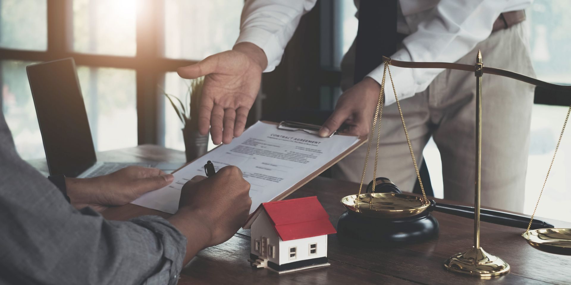 People reviewing a house document over a desk with a small red-roof model house and scale in the foreground