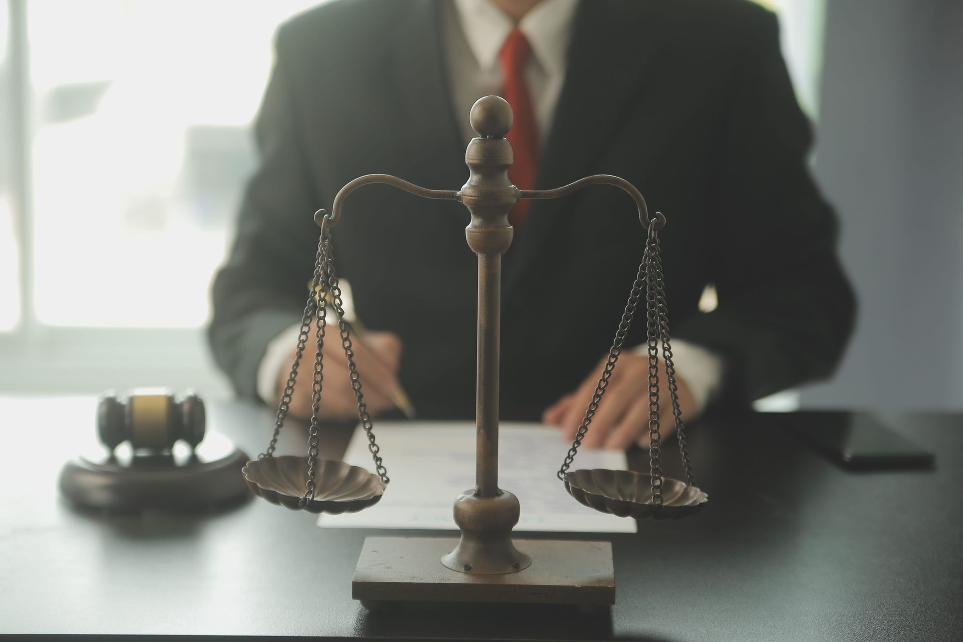Scales of justice on a desk with a blurred lawyer in a suit and gavel in the background