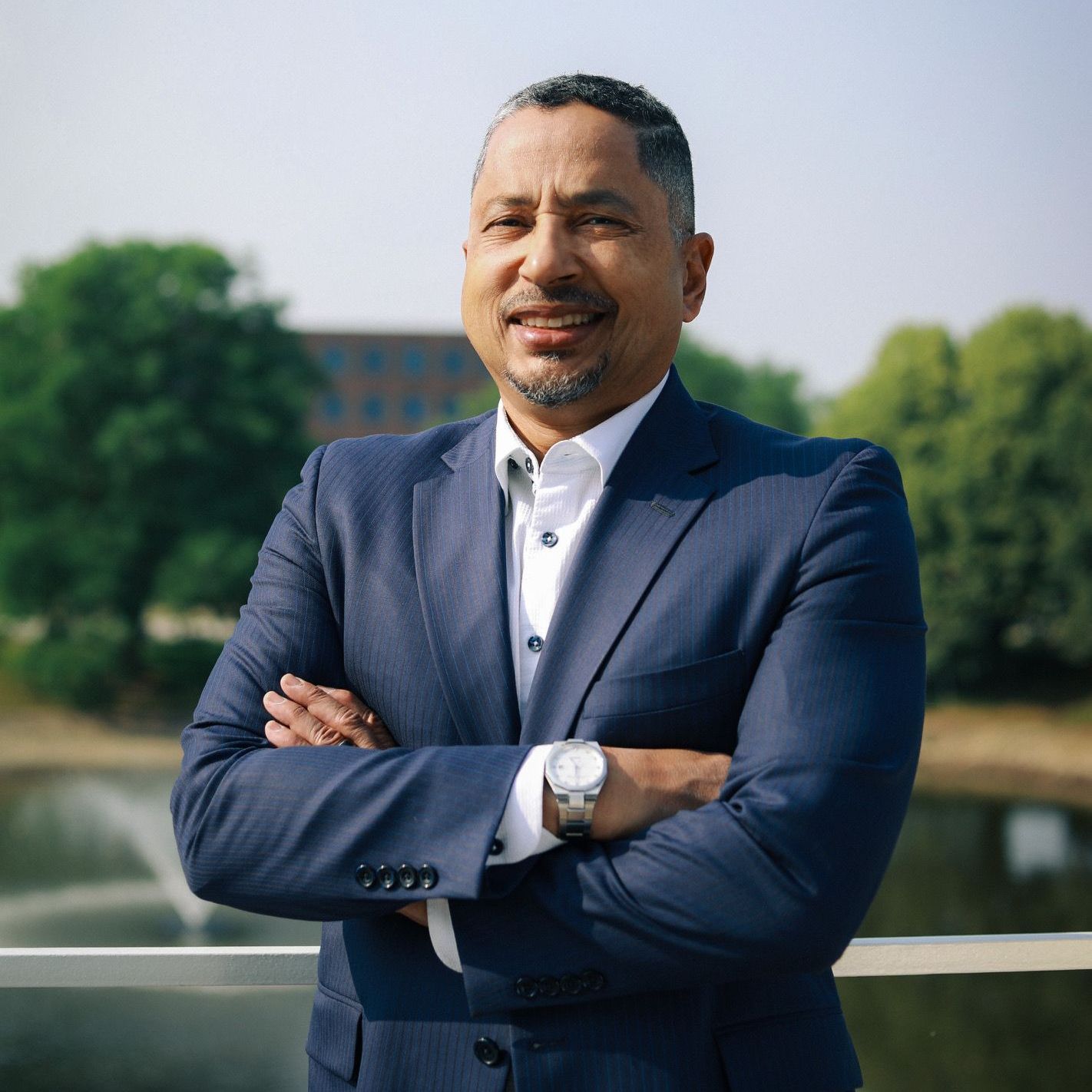 A man in a blue suit and white shirt is standing with his arms crossed.