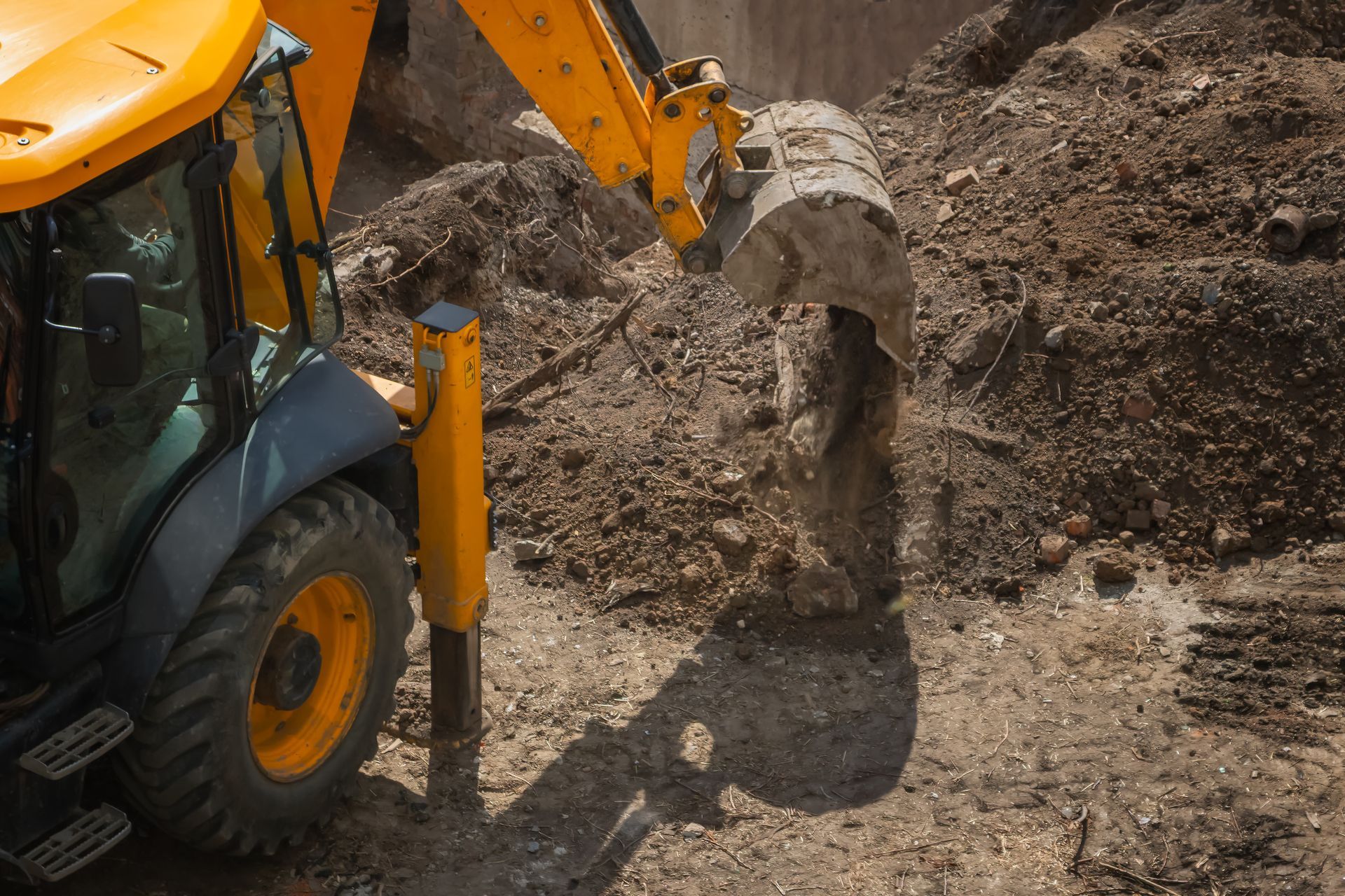 Yellow excavator dumping dirt at a construction site with a muddy pile.