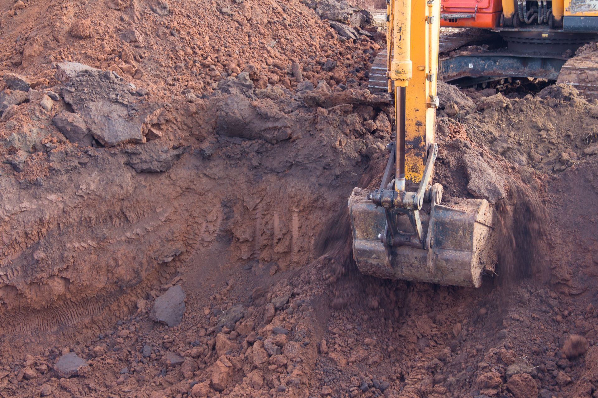 Excavator bucket digging reddish soil at a construction site