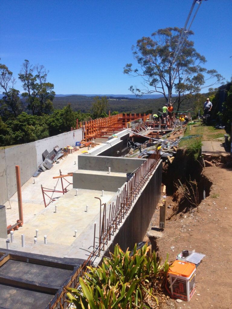 Partially built concrete foundation on a hillside with scaffolding and construction materials, overlooking a valley