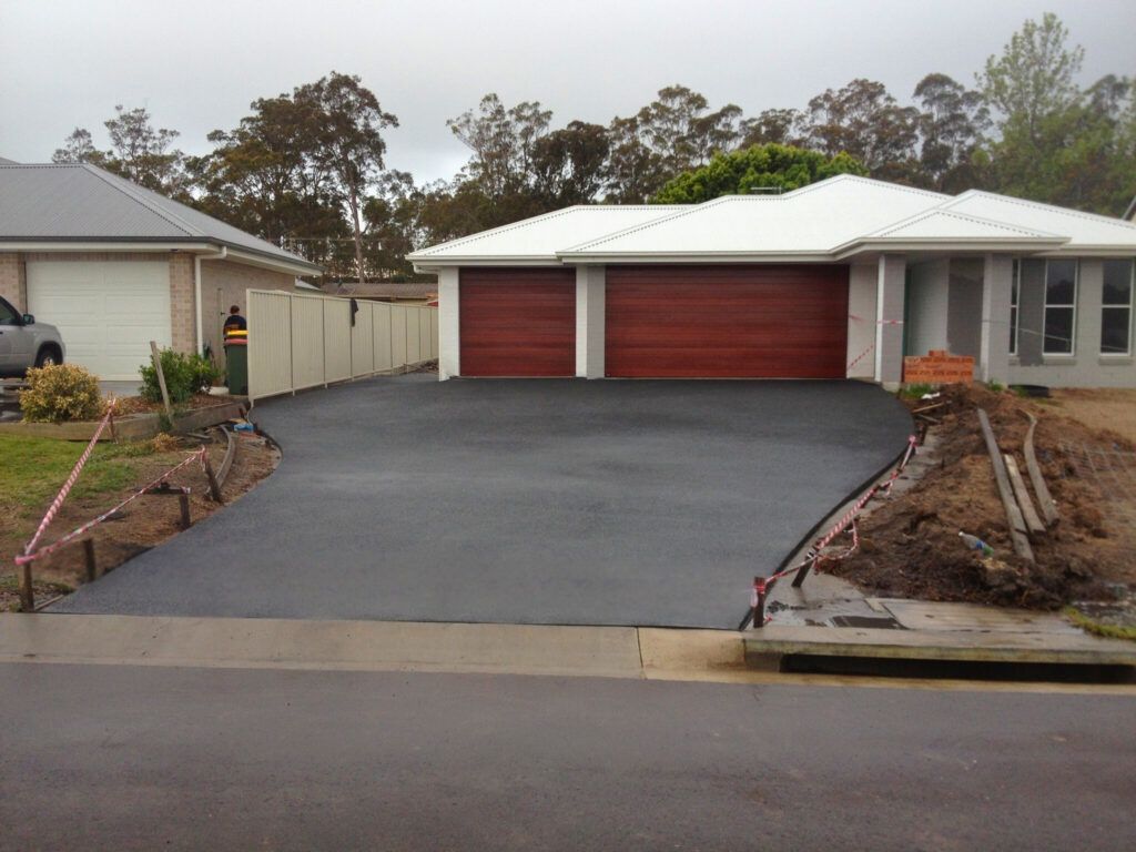 Newly paved black driveway leading to a red double garage with a white roof in a suburban home