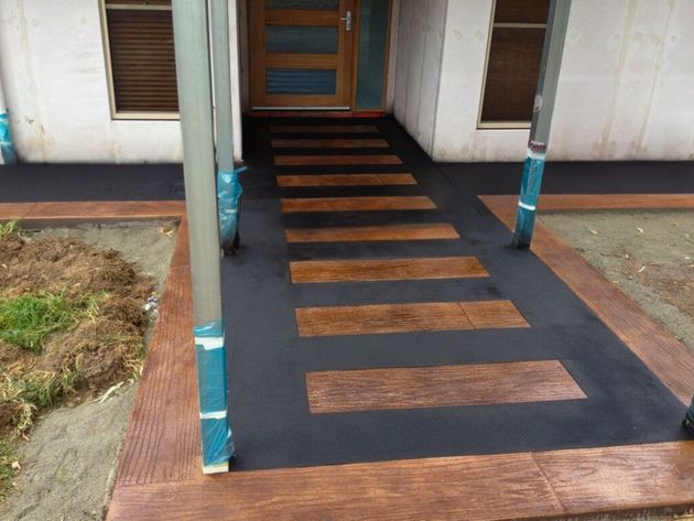 Front porch ramp with black surface and wooden slats leading to a doorway of a house