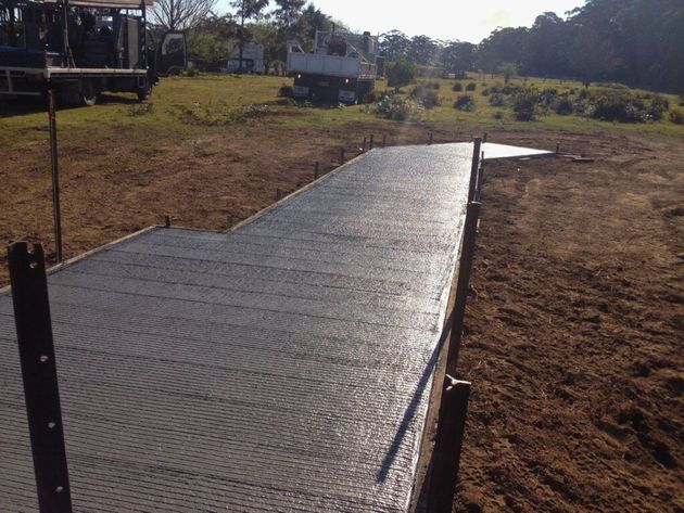 Freshly poured concrete walkway across a dry grassy field under construction