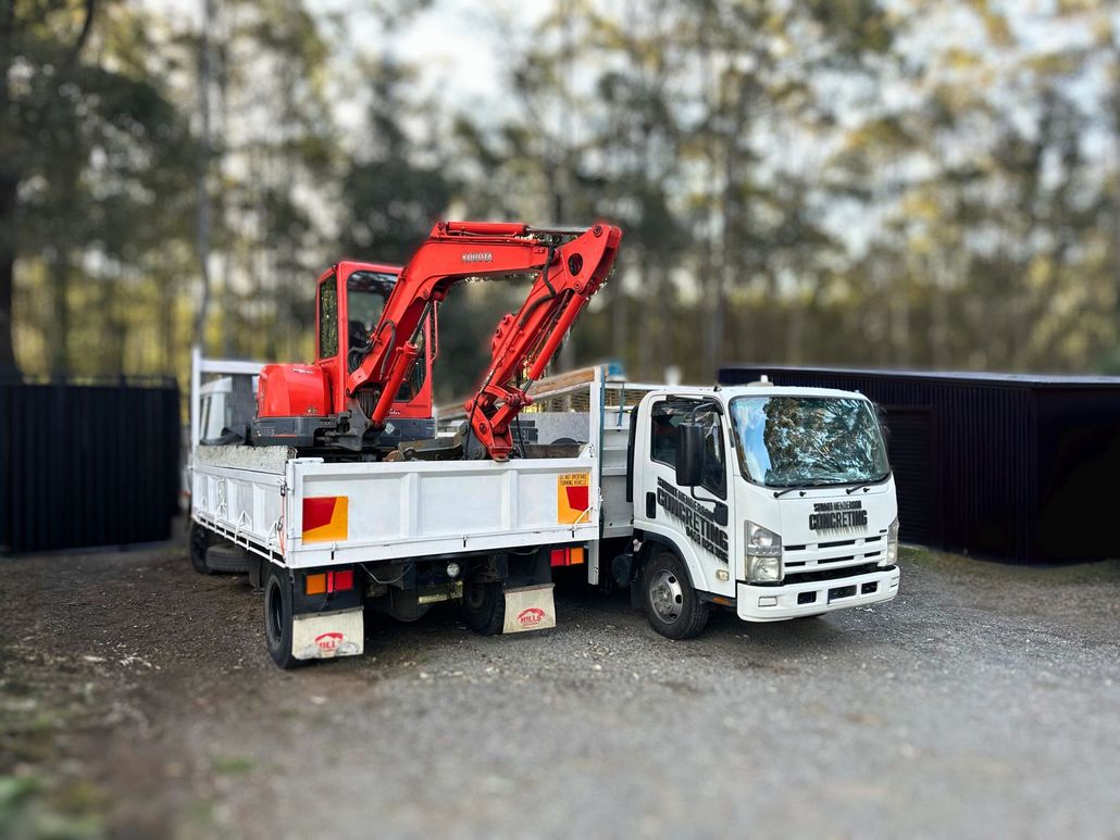 Red flatbed truck with a folded red crane parked beside a white truck on gravel.